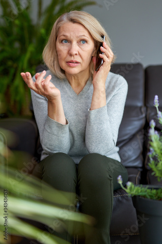 Serious woman attending a phone call sitting on a sofa in the living room at home