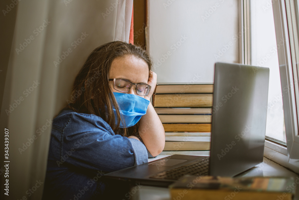 man with glasses and a blue medical mask sleeps in front of a laptop. tired student with glasses fell asleep while studying at home during quarantine man with glasses and a blue medical mask sleeps in front of a laptop. tired student with glasses fell asleep while studying at home during quarantine