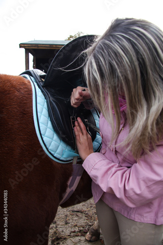 girl with horse tightening the girth on a saddle.  photo