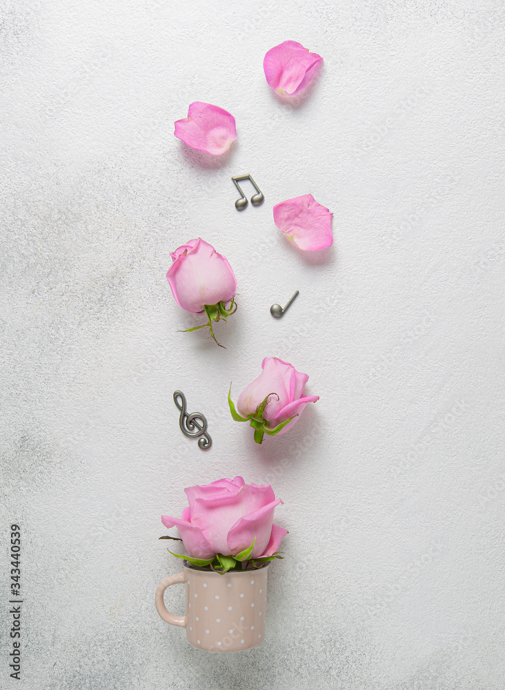 Romantic card with pink rose buds and metal miniature of notes on light background.Top view. Romantic card with pink rose buds and metal miniature of notes on light background.Top view.