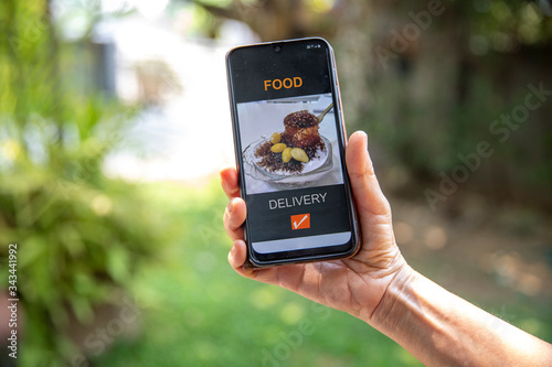 Woman hand holding mobile phone with open page of food delivery service online at home