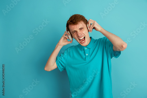 Listen to music, crazy. Caucasian young man's modern portrait isolated on blue studio background, monochrome. Beautiful male model. Concept of human emotions, facial expression, sales, ad, trendy.