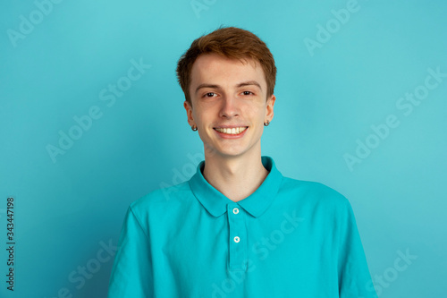 Smiling calm and happy. Caucasian young man's modern portrait isolated on blue studio background, monochrome. Beautiful male model. Concept of human emotions, facial expression, sales, ad, trendy.