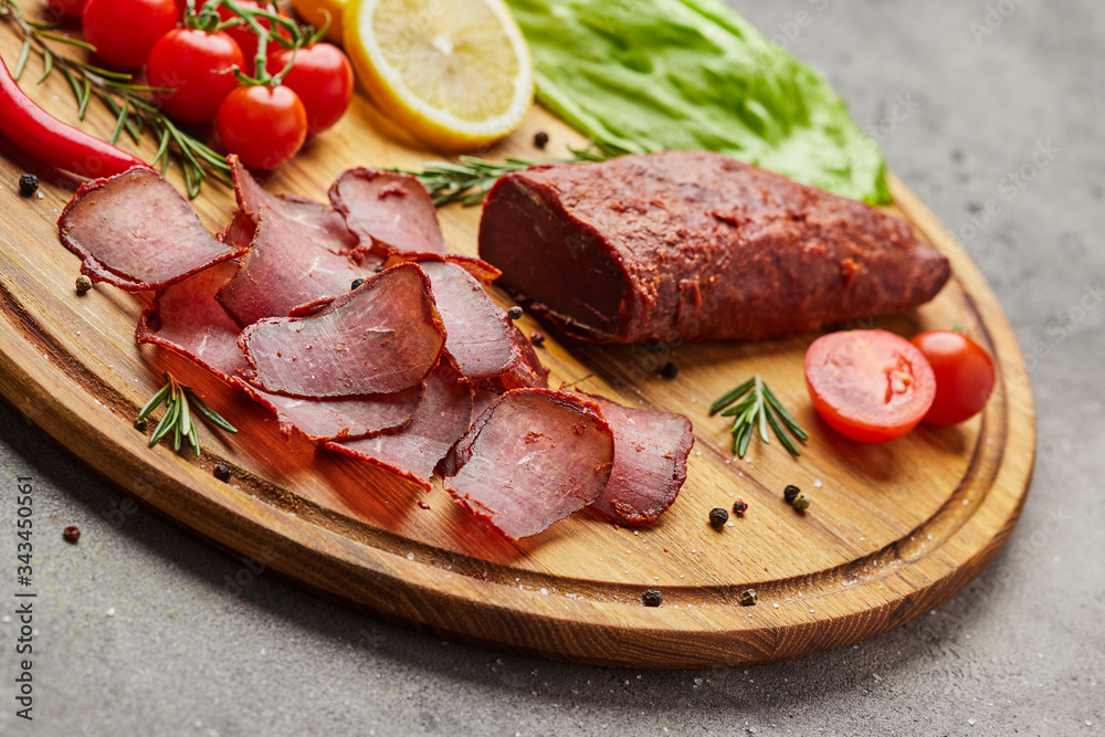 Armenian basturma or Pastirma on wooden cutting board decorated with spices, lettuce, lemon and tomatoes. Meat smoked jerky good as Beer snack Armenian basturma or Pastirma on wooden cutting board decorated with spices, lettuce, lemon and tomatoes. Meat smoked jerky good as Beer snack