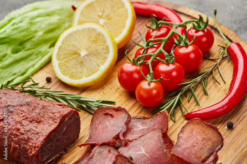 Armenian basturma or Pastirma on wooden cutting board decorated with spices, lettuce, lemon and tomatoes. Meat smoked jerky good as Beer snack