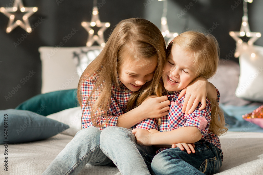two sisters in plaid shirts and jeans sit on bed. two sisters in plaid shirts and jeans sit on bed.