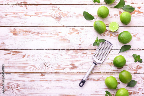 Fresh limes with grater on white wooden background