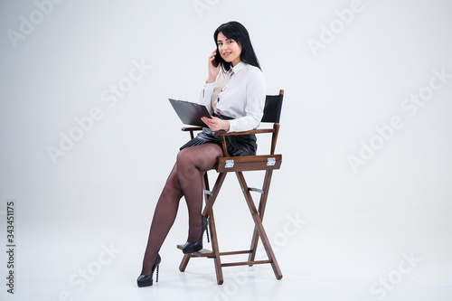 Successful business woman in a white shirt sitting on a chair with documents and talking about the business on the phone.