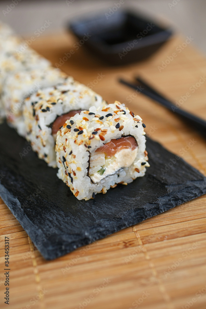 Japanese sushi rolls sprinkled with sesame seeds on a black stone board.