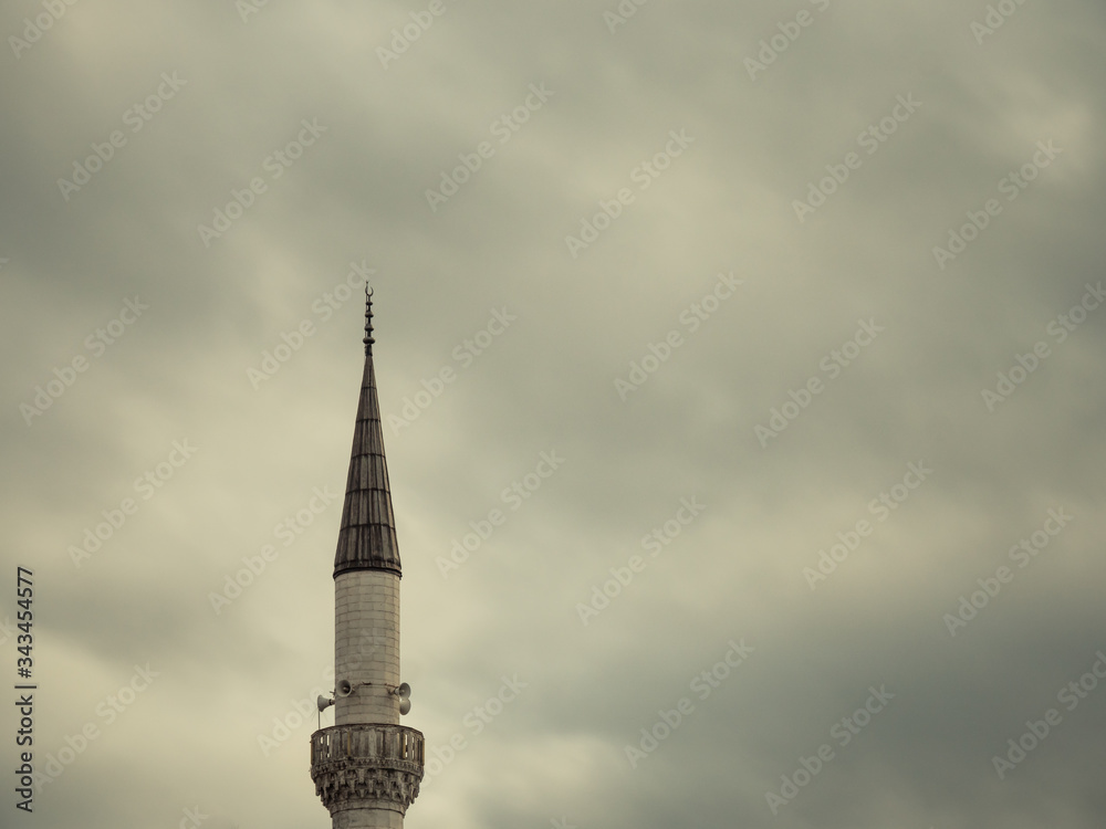 Minaret of a Muslim mosque on the background of the cloudy sky.