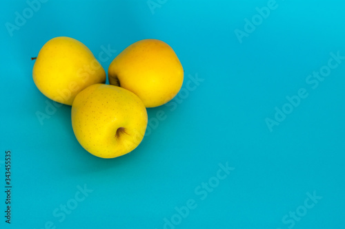 Three yellow apples on a blue background. Blue background with space for text. Minimalist design. An isolated group of three apples . Golden apples are on the table.