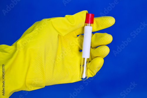 Hand in yellow medical rubber gloves holding tube with tuffer for analysis on blue background. photo