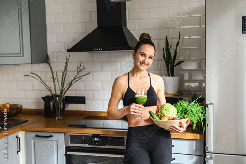 Vegetable smoothie detox in the hands of a young woman, she is in sportswear in the kitchen photo