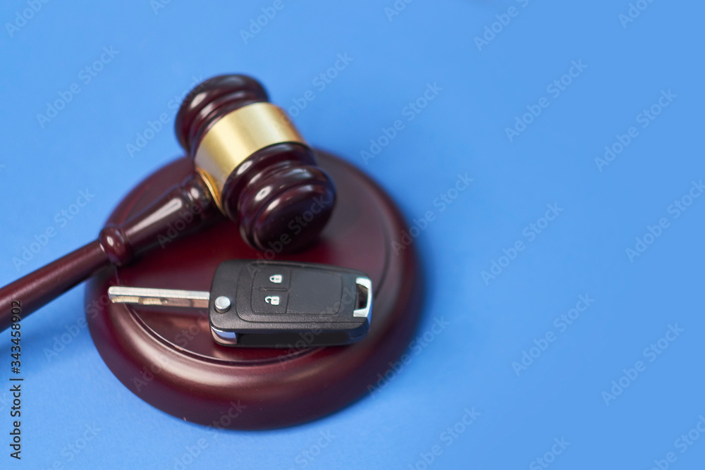 Close up of judge gavel and car keys over soundboard on blue background.