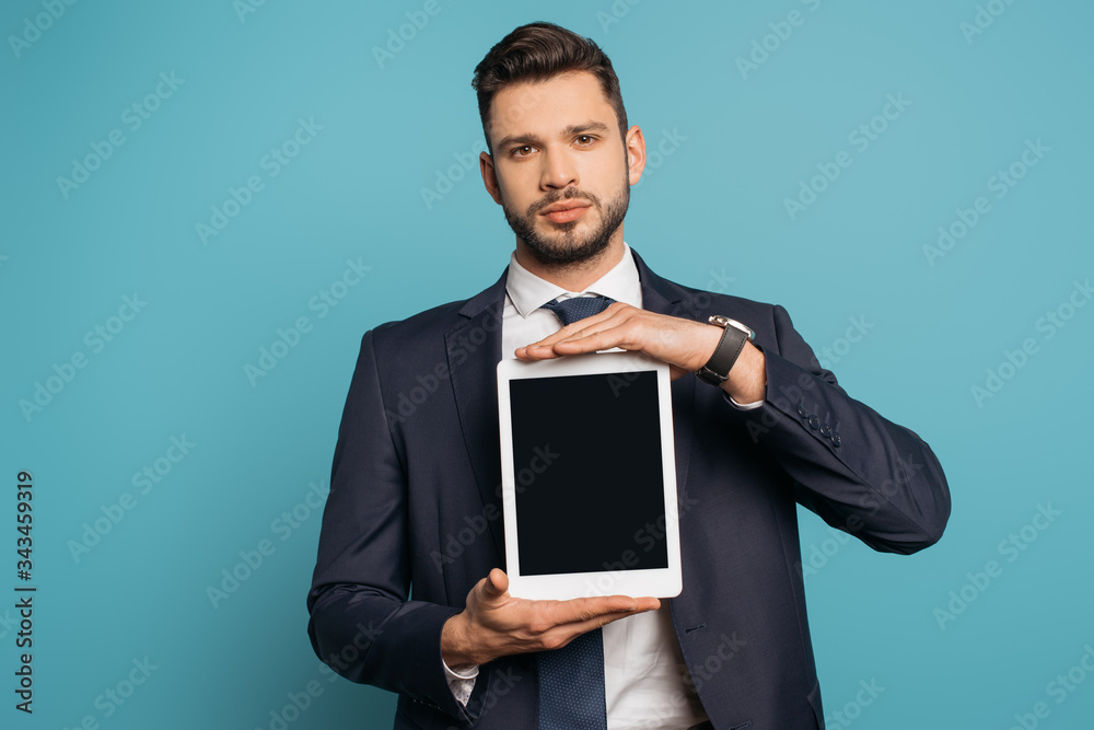 confident businessman showing digital tablet with blank screen while looking at camera on blue background confident businessman showing digital tablet with blank screen while looking at camera on blue background