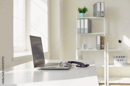 Doctor online. A stethoscope is on a white table with a laptop in blur at the hospital office.