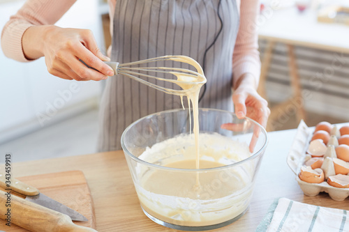 Fototapeta Unrecognizable woman making dough for cupcakes using whip, horizontal high angle