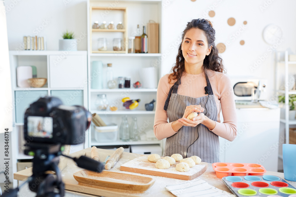 Attractive food vlogger preparing dough for baking it while shooting video on camera Attractive food vlogger preparing dough for baking it while shooting video on camera