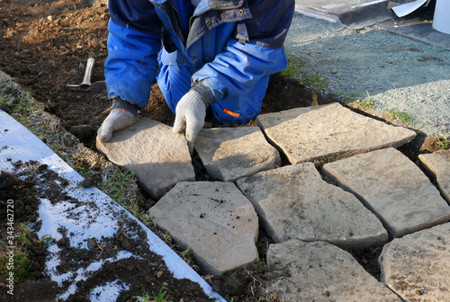 Hands hits a stone with a hammer to make it fit and to place stone pavers