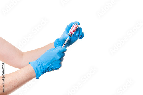 hands in blue medical gloves are holding a glass bottle with a vaccine pink pills a drug into an injection syringe, medical theme close up isolated on white background with copy space.
