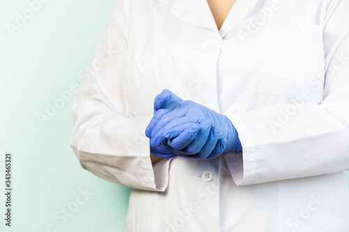 A woman wears medical gloves standing against a blue background in a white uniform. Selective focus