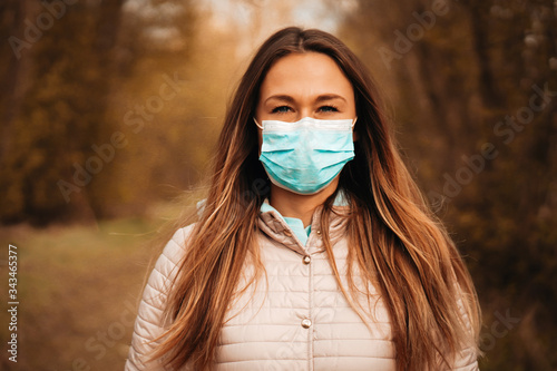 Portrait of a young brown-haired woman on blurred background in the nature. She is wearing a protective face mask and thinking when the corona virus - COVID 19 and the quarantine will end.