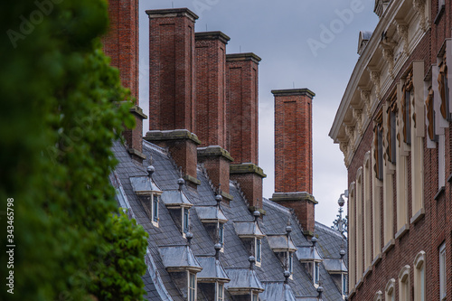 Scorcio panoramico di un tipico tetto olandese in ardesia con finestre e alte canne fumarie in mattoni e parte di un edificio adiacente photo