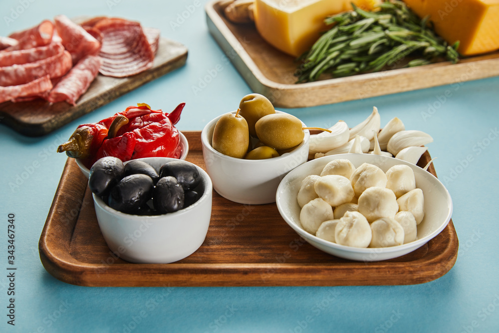 Selective focus of antipasto ingredients on boards on blue background