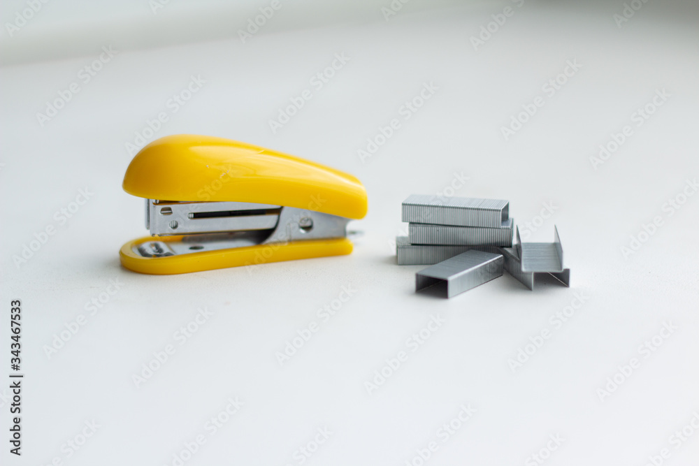 Yellow small stapler on a white background. Stapler staples are located nearby. Yellow small stapler on a white background. Stapler staples are located nearby.