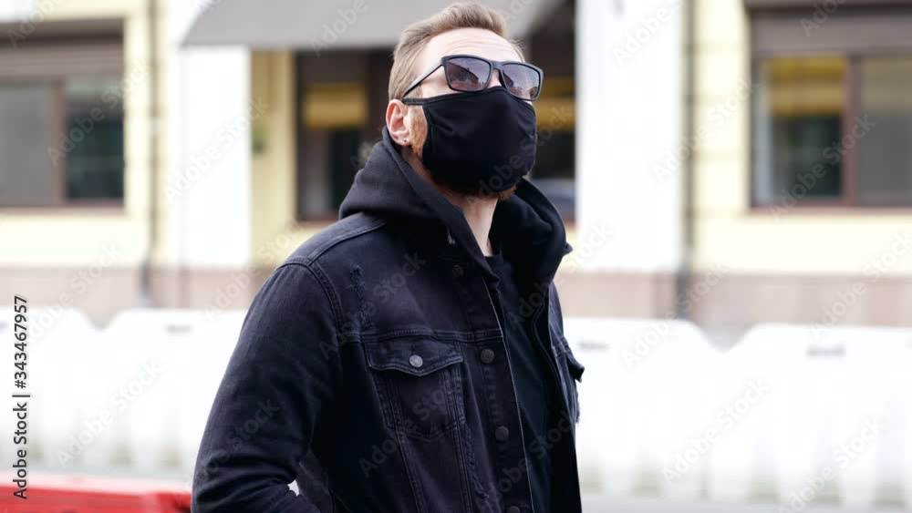 Man wearing balck face mask and walking at the street. Looking aside. Handheld shot. Man wearing balck face mask and walking at the street. Looking aside. Handheld shot.