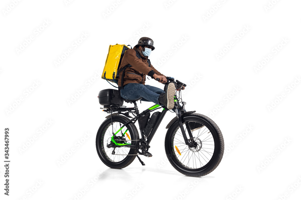 Naklejka premium Too much orders. Contacless delivery service during quarantine. Man delivers food during isolation, wearing helmet and face mask. Taking food on bike isolated on white background. Safety. Hurrying up.