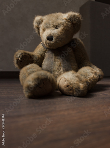 toy of a lonely teddy bear sits on a dark wooden floor