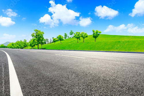 Empty asphalt road and green grass with tree under the blue sky.