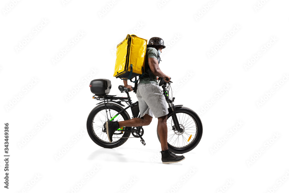 Too much orders. Contacless delivery service during quarantine. Man delivers food during isolation, wearing helmet and face mask. Taking food on bike isolated on white background. Safety. Hurrying up.