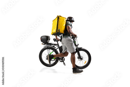 Fototapeta Naklejka Na Ścianę i Meble -  Too much orders. Contacless delivery service during quarantine. Man delivers food during isolation, wearing helmet and face mask. Taking food on bike isolated on white background. Safety. Hurrying up.