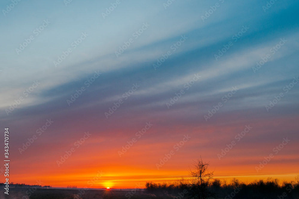 Panorama of dawn fire in the sky above the natural pasture. Golden red clouds just before sunrise. Picturesque landscape at sunrise. Beauty in nature