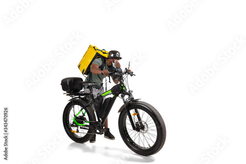Too much orders. Contacless delivery service during quarantine. Man delivers food during isolation  wearing helmet and face mask. Taking food on bike isolated on white background. Safety. Hurrying up.