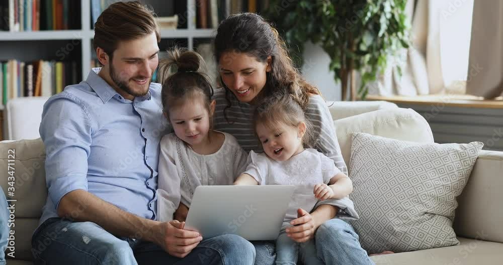 Cute small kids learning using computer looking at laptop screen sit on parents lap on sofa. Happy family enjoying watching children distance education video, doing online shopping on website at home.
