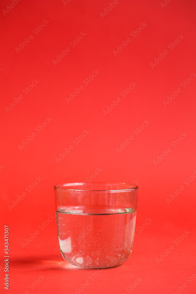 Transparent glass of water on a red background