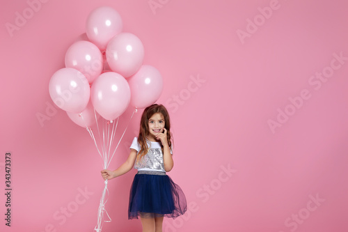 Smiling adorable little child girl posing with pastel pink air balloons isolated over pink background. Beautiful happy kid on a birthday party. copy space
