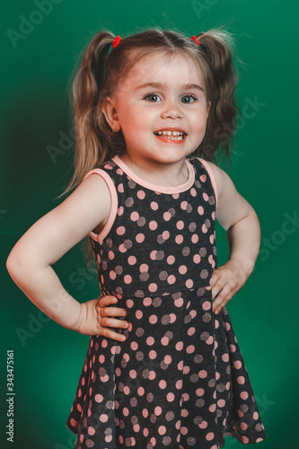 Little girl of three years with tails in dress posing in studio on green background