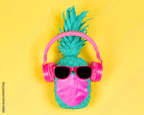 Pineapple in pink headphones and medical mask on a yellow background