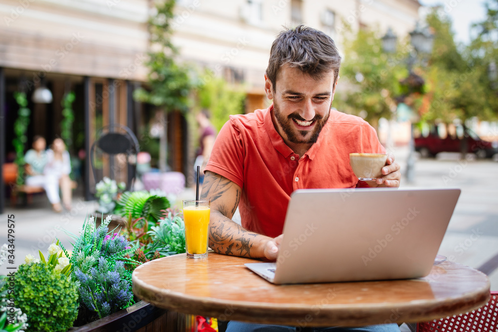 Young man having fun, enjoying free time on laptop and smiling while sitting in cafe Young man having fun, enjoying free time on laptop and smiling while sitting in cafe