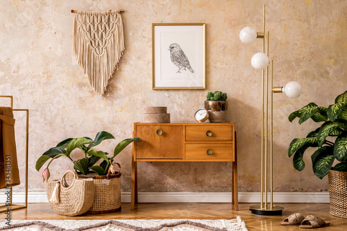 Modern retro composition of living room with wooden vintage commode, furniture, lamp, plant, carpet, pillows, gold mock up poster frame, plants, decoration and personal accessories. photo