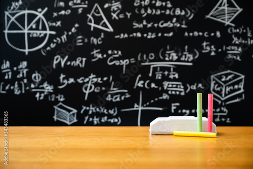 Education background concept. Board eraser and chalk on the wooden table with blackboard with many Mathematical formula.