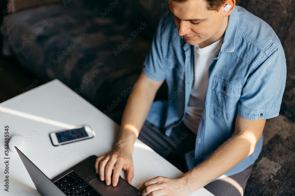 Handsome young man using laptop and headphones at home. Student men resting in his room. Online webinar, home work, freelance, online learning, studying concept. Distance education