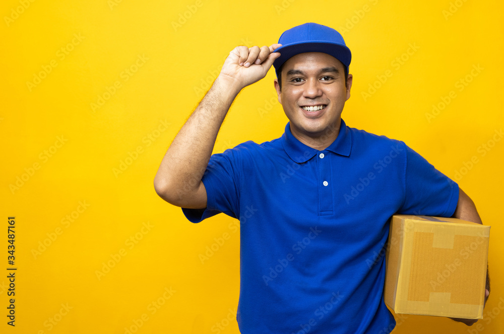 Blue Delivery handsome asian man holding parcel cardboard box on isolated yellow background.