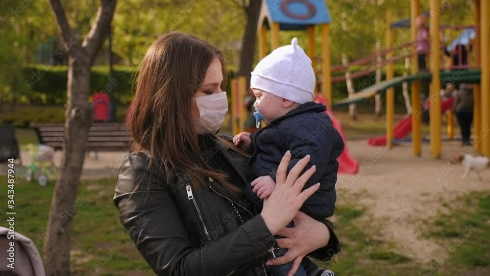 Portrait of a young mother in a medical mask with a small child in the Park on the Playground. Quarantine for the coronavirus. Covid-19. Portrait of a young mother in a medical mask with a small child in the Park on the Playground. Quarantine for the coronavirus. Covid-19.