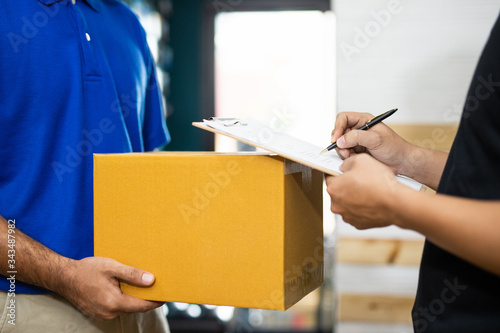 Delivery man sending parcel cardboard box to customer and signing receipt of delivery package.