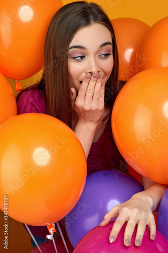 Smiling surprised caucasian girl posing with bright color air balloons on yellow background. Beautiful happy young woman on a birthday holiday. close-up